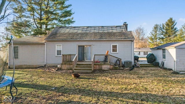 rear view of house with central AC unit, a wooden deck, a chimney, a trampoline, and a lawn