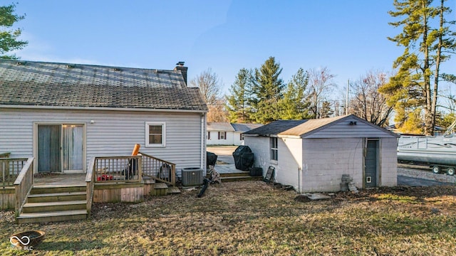 back of house featuring a chimney, an outdoor structure, a deck, and a shingled roof