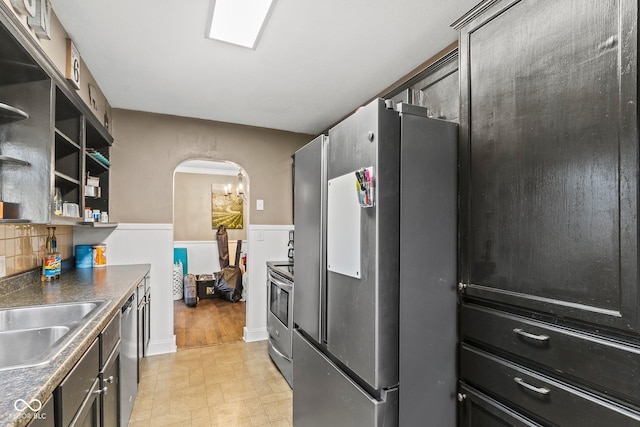 kitchen featuring dark countertops, a sink, arched walkways, stainless steel appliances, and open shelves