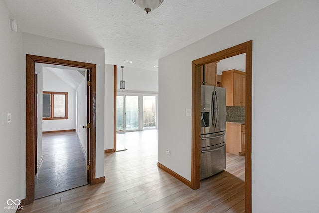 corridor featuring light wood-style flooring, a textured ceiling, and baseboards