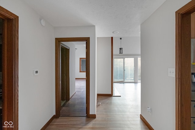 hall with baseboards, light wood-style floors, and a textured ceiling