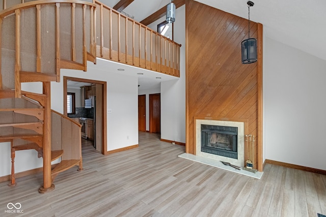 unfurnished living room with a fireplace with raised hearth, high vaulted ceiling, stairs, and wood finished floors