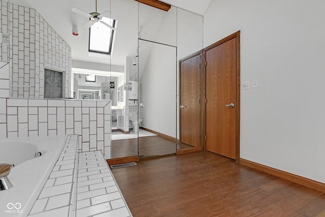 full bath featuring visible vents, vaulted ceiling with skylight, wood finished floors, a bath, and a ceiling fan