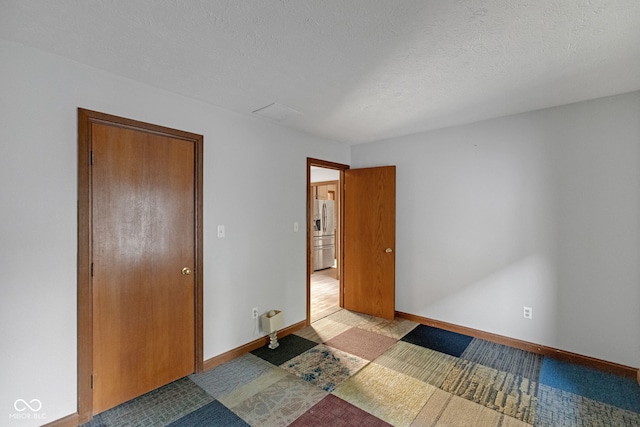 unfurnished bedroom with a textured ceiling, baseboards, and stainless steel refrigerator with ice dispenser