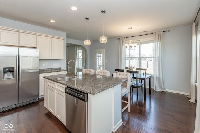 kitchen with a center island with sink, a breakfast bar, arched walkways, a sink, and stainless steel appliances