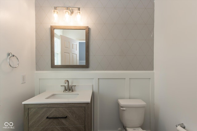 bathroom featuring a decorative wall, toilet, and vanity