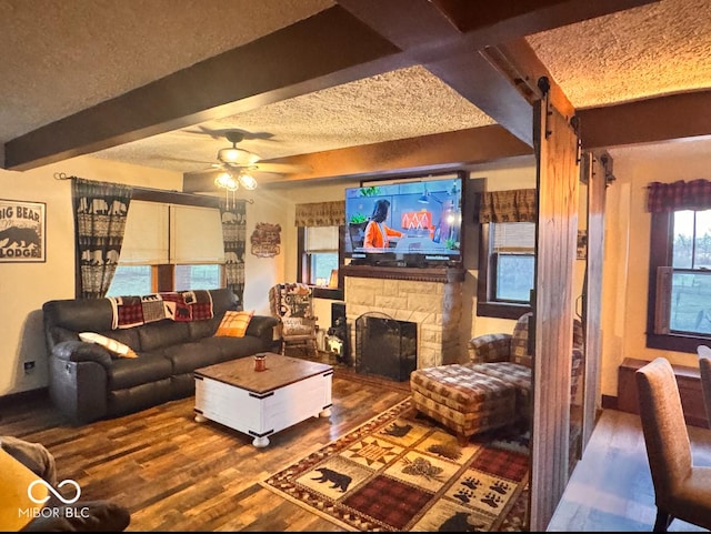 living room featuring beam ceiling, a fireplace, wood finished floors, a textured ceiling, and a ceiling fan