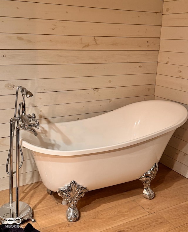 full bathroom with wood walls, a freestanding bath, and wood finished floors