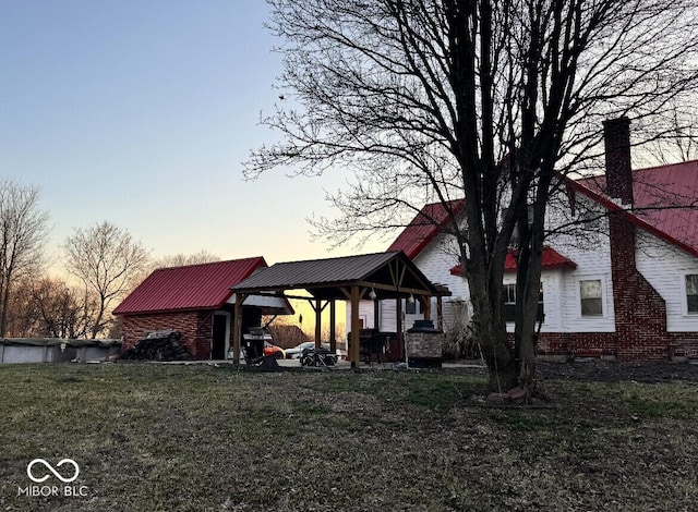 back of house at dusk with a gazebo, a lawn, and metal roof