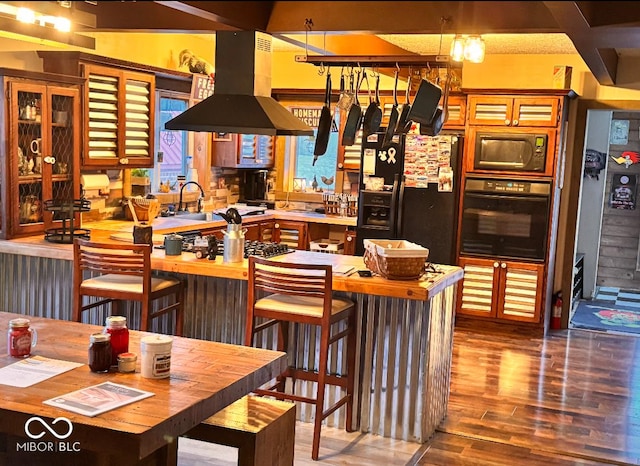 kitchen with a sink, black appliances, wood finished floors, and island range hood