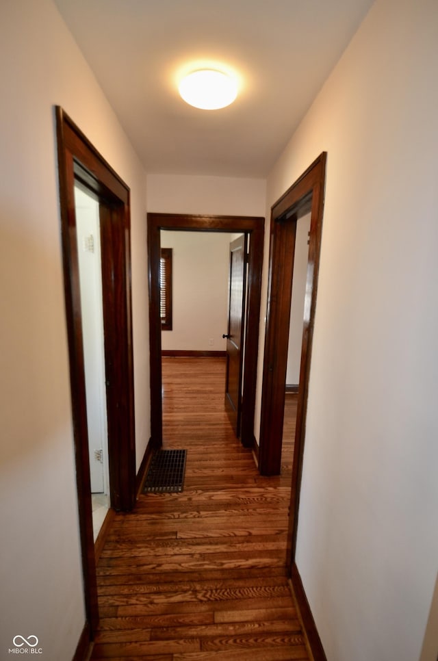 hallway featuring visible vents, baseboards, and dark wood finished floors