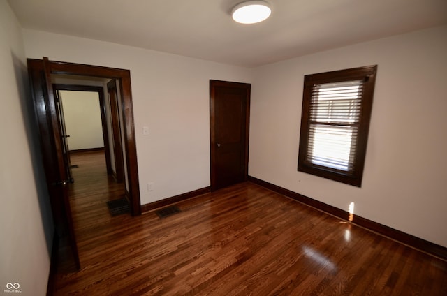 unfurnished bedroom with visible vents, baseboards, dark wood-style flooring, and a closet