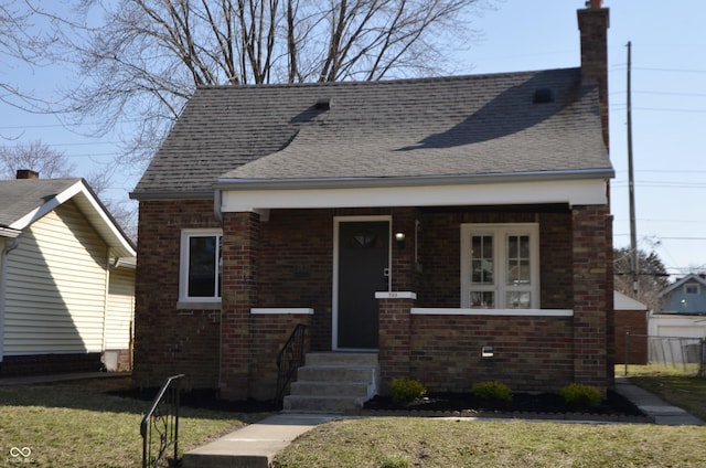 bungalow-style house with brick siding, a front yard, and a shingled roof