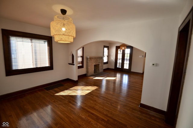 unfurnished living room featuring a stone fireplace, wood finished floors, arched walkways, and baseboards