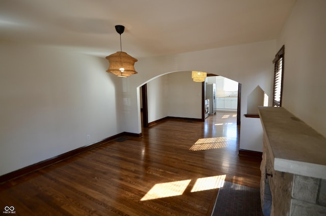 unfurnished dining area with baseboards, arched walkways, and wood finished floors