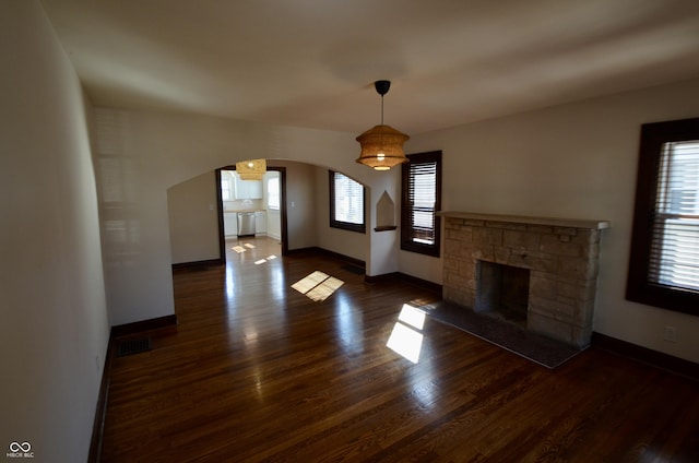 unfurnished living room with arched walkways, visible vents, a healthy amount of sunlight, and wood finished floors