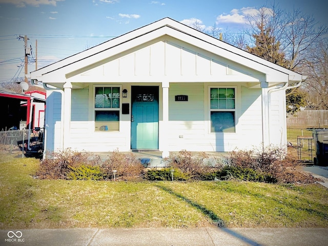 bungalow-style house with covered porch, board and batten siding, a front yard, and fence