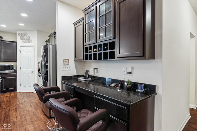 kitchen with dark stone countertops, recessed lighting, stainless steel appliances, glass insert cabinets, and dark wood-style flooring