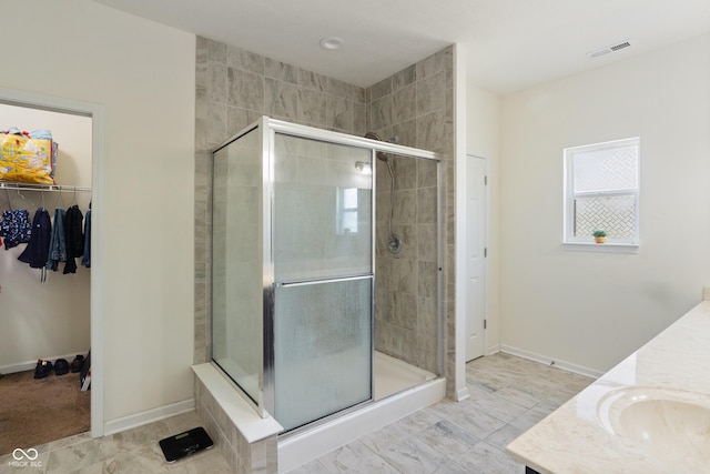 full bath with visible vents, a walk in closet, baseboards, a stall shower, and vanity