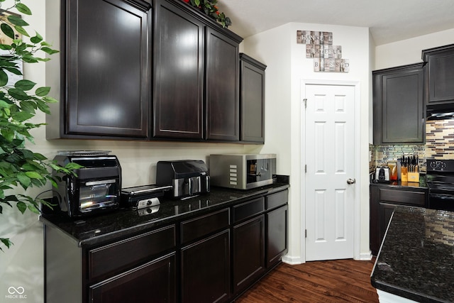 kitchen with stainless steel microwave, dark wood-style floors, black range with electric cooktop, dark stone counters, and decorative backsplash