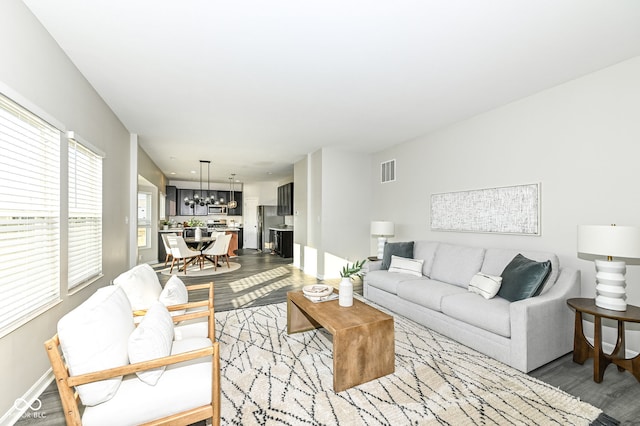 living room with visible vents, baseboards, an inviting chandelier, and wood finished floors