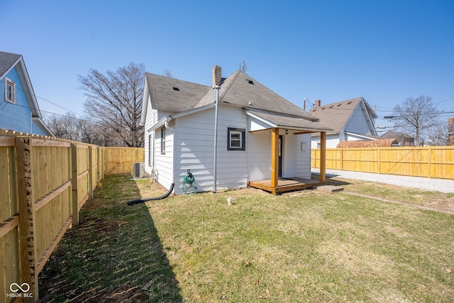 rear view of house with central AC unit, a lawn, a fenced backyard, and roof with shingles