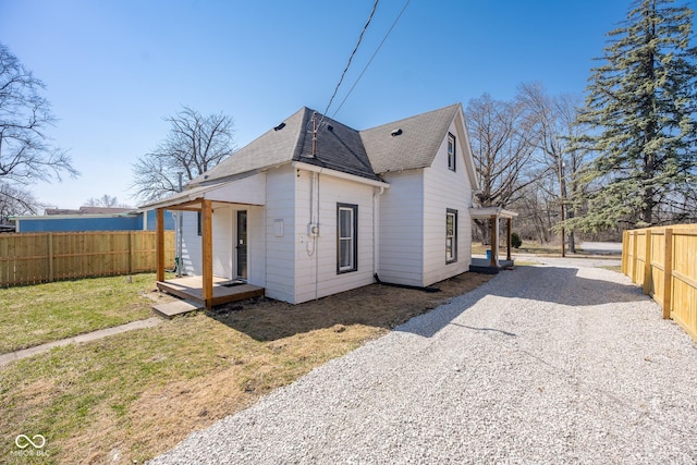 exterior space with a yard, fence, driveway, and a shingled roof