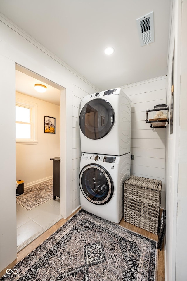 washroom featuring visible vents, laundry area, stacked washer / drying machine, and wooden walls