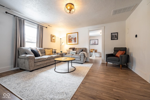 living area featuring baseboards, wood finished floors, visible vents, and a textured ceiling