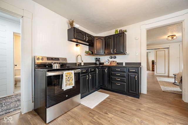 kitchen with a sink, light wood-style floors, dark countertops, and stainless steel range with electric cooktop