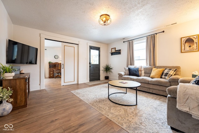 living room with visible vents, baseboards, a textured ceiling, and wood finished floors