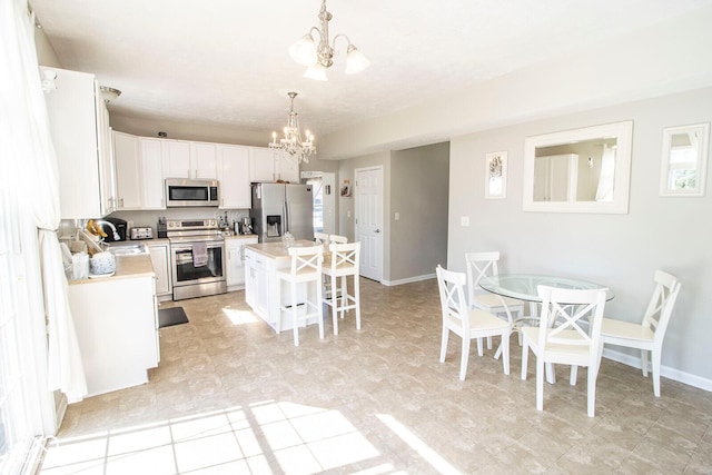 kitchen with a kitchen bar, white cabinetry, appliances with stainless steel finishes, light countertops, and a chandelier