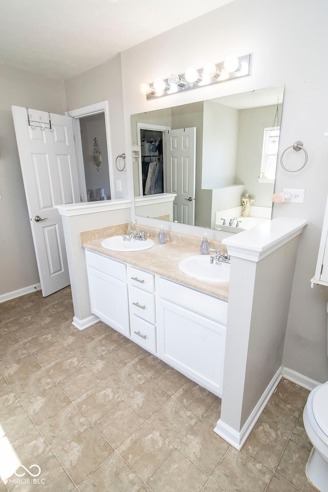 full bath with a sink, a walk in closet, baseboards, and double vanity