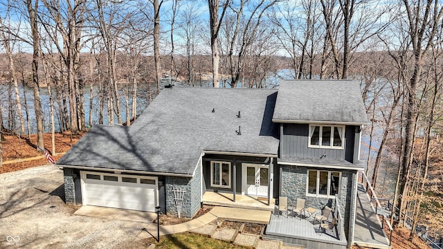 view of front of home with driveway, stone siding, french doors, an attached garage, and a shingled roof