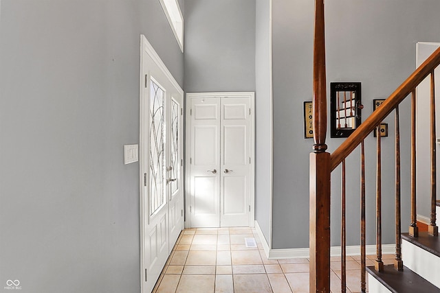 entrance foyer featuring light tile patterned floors, baseboards, stairs, and a towering ceiling