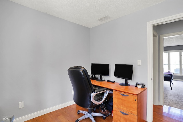 office featuring visible vents, a textured ceiling, baseboards, and wood finished floors