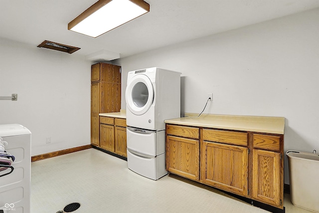 laundry room featuring cabinet space, stacked washer and clothes dryer, light floors, and baseboards