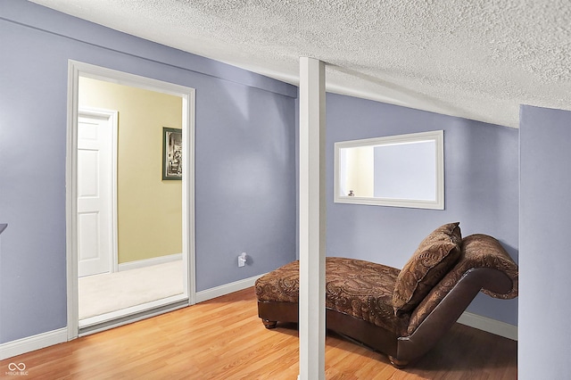 living area with vaulted ceiling, wood finished floors, baseboards, and a textured ceiling