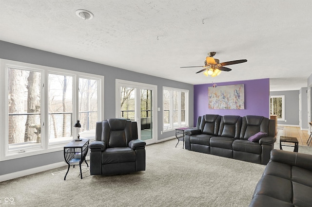 carpeted living area featuring baseboards, plenty of natural light, and a ceiling fan