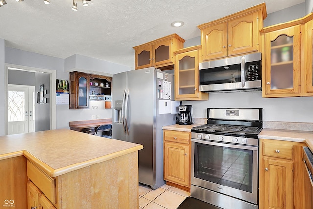 kitchen featuring a textured ceiling, stainless steel appliances, light countertops, light tile patterned floors, and glass insert cabinets