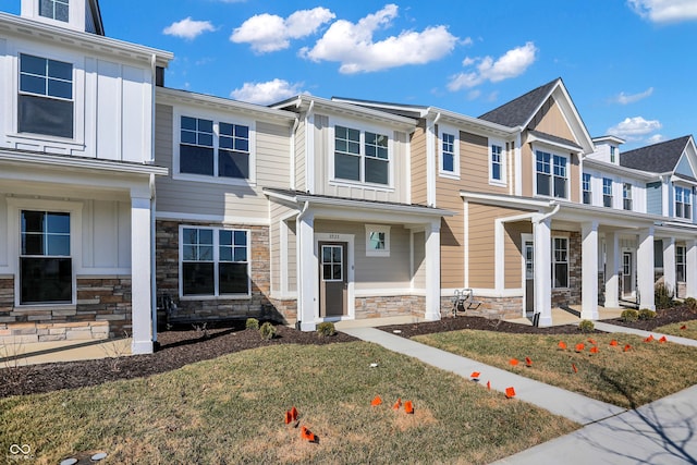 townhome / multi-family property with board and batten siding, a front yard, a porch, and stone siding