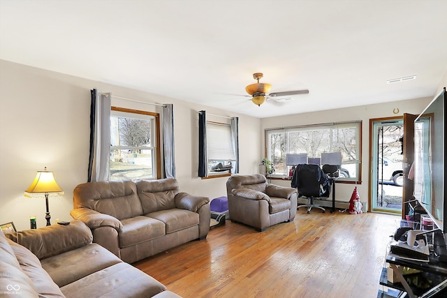 living area with a wealth of natural light, light wood-type flooring, and a ceiling fan