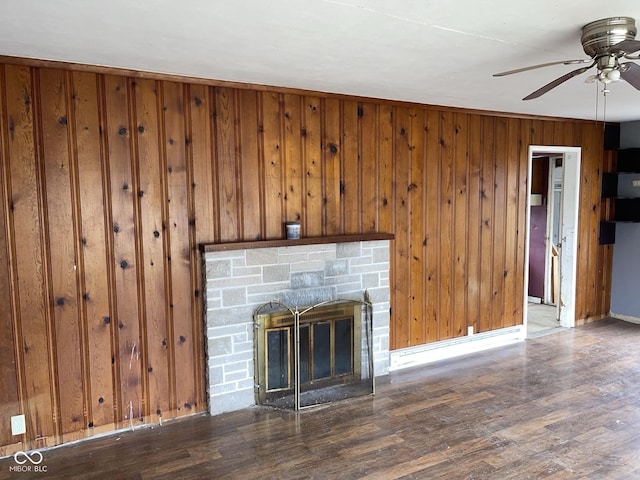 unfurnished living room with wooden walls, a stone fireplace, a ceiling fan, and wood finished floors