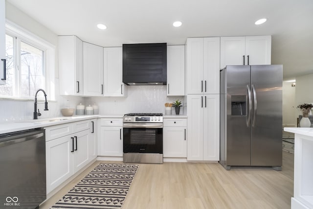 kitchen with a sink, light countertops, white cabinets, appliances with stainless steel finishes, and wall chimney range hood