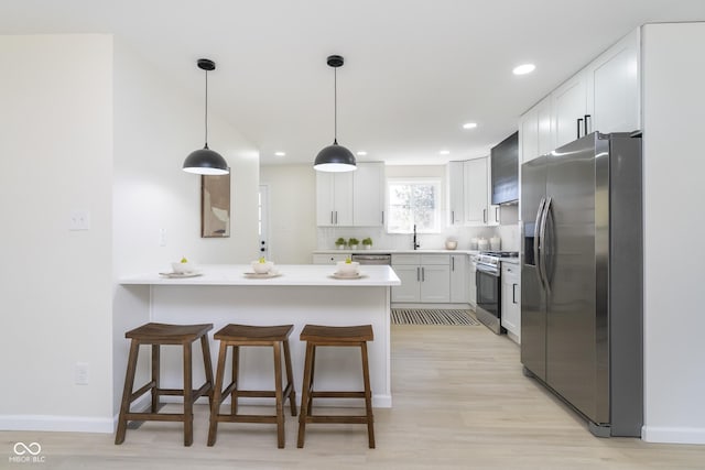 kitchen featuring a peninsula, light countertops, white cabinets, appliances with stainless steel finishes, and a kitchen breakfast bar