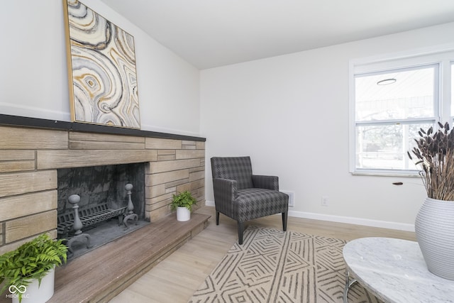 living area with baseboards, a fireplace with raised hearth, and light wood finished floors