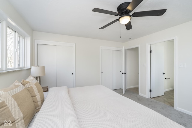 bedroom featuring a ceiling fan, light colored carpet, multiple closets, and baseboards