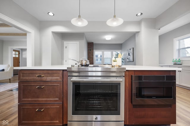 kitchen with open floor plan, light countertops, stainless steel range with electric stovetop, light wood-style floors, and hanging light fixtures