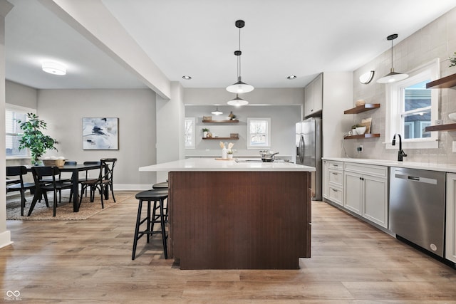 kitchen with open shelves, backsplash, stainless steel appliances, light wood finished floors, and light countertops