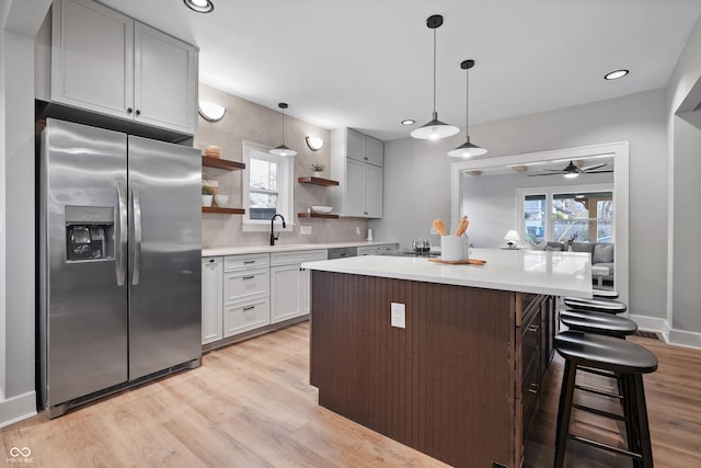 kitchen featuring a sink, stainless steel fridge, light countertops, and open shelves